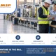 Counting the cost of manufacturing cyberattack downtime — an idle but orderly production line while a plant manager and an IT lead review a recovery plan on a clipboard and tablet at a floor workstation